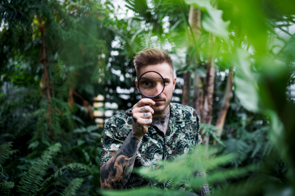 Young man researcher with magnifying glass standing in botanical garden.