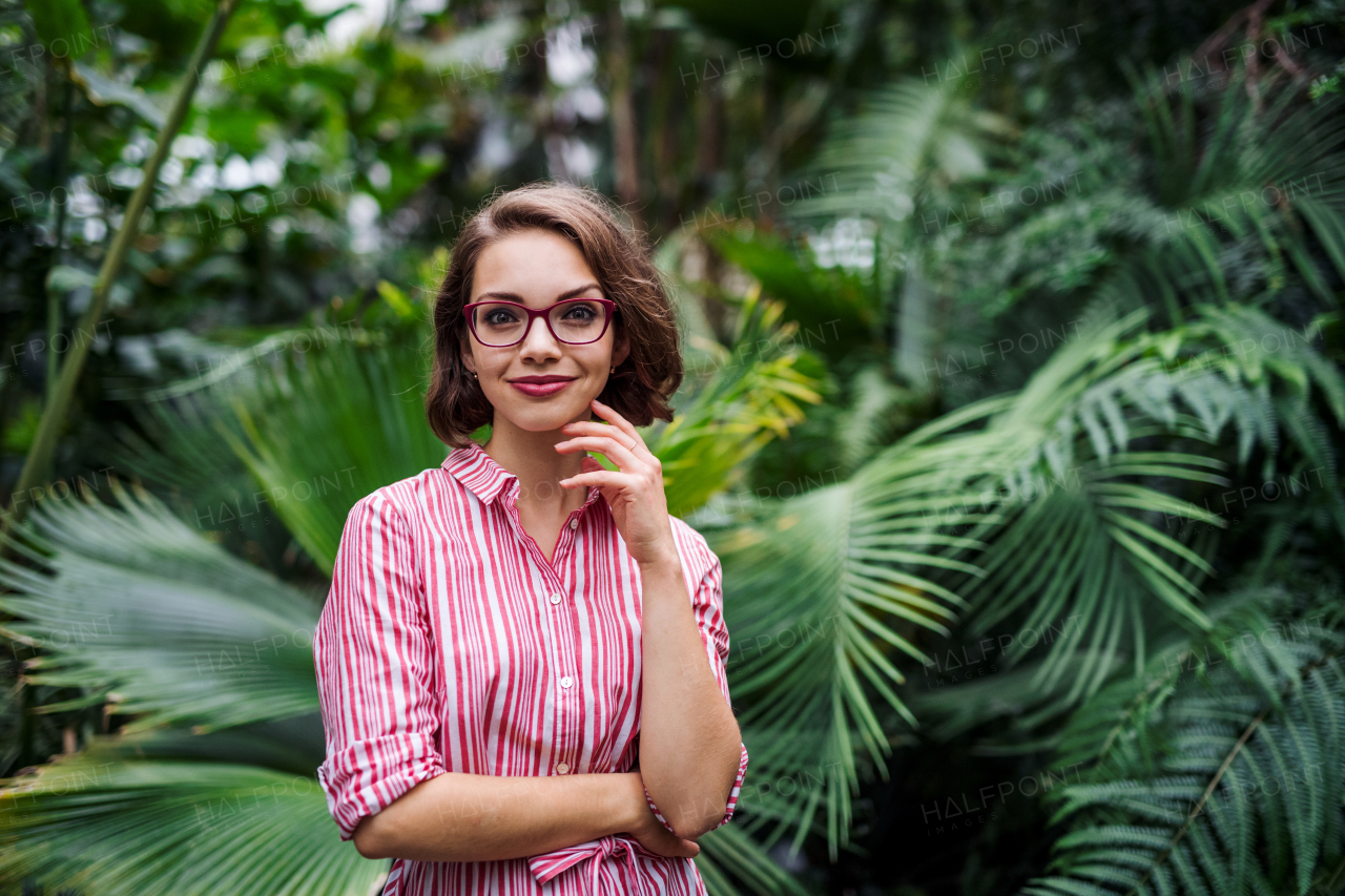 Young woman with arms crossed standing in botanical garden, looking at camera.