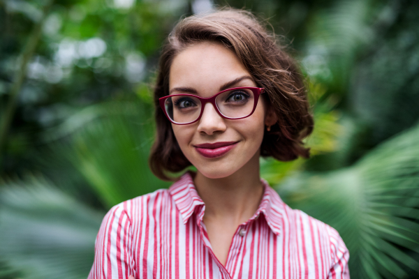 Young woman with arms crossed standing in botanical garden, looking at camera.