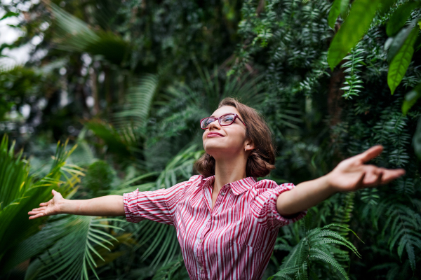 A young woman standing in botanical garden, arms stretched.