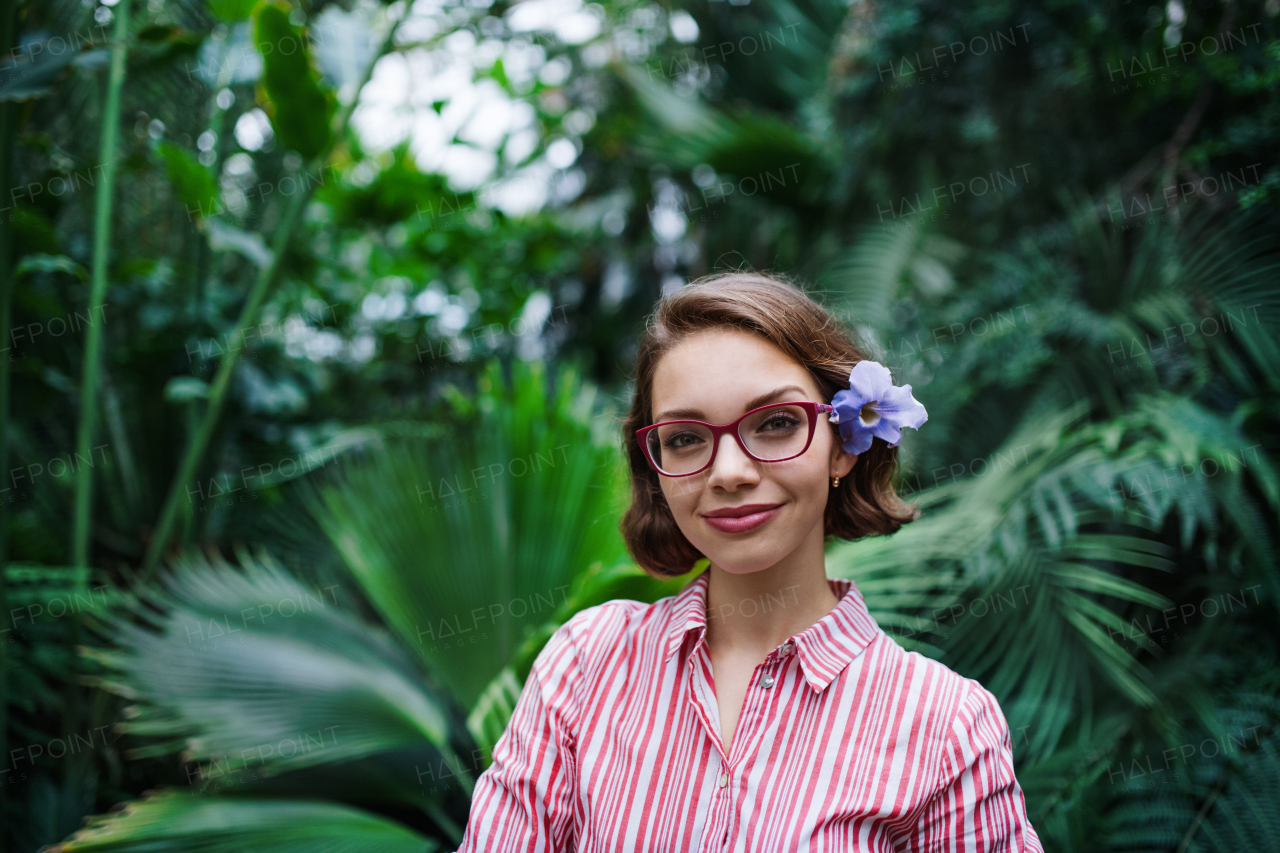 Beautiful young woman standing in botanical garden, looking at camera.