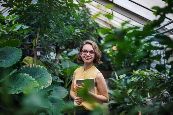 Young woman with tablet standing in greenhouse in botanical garden. Copy space.