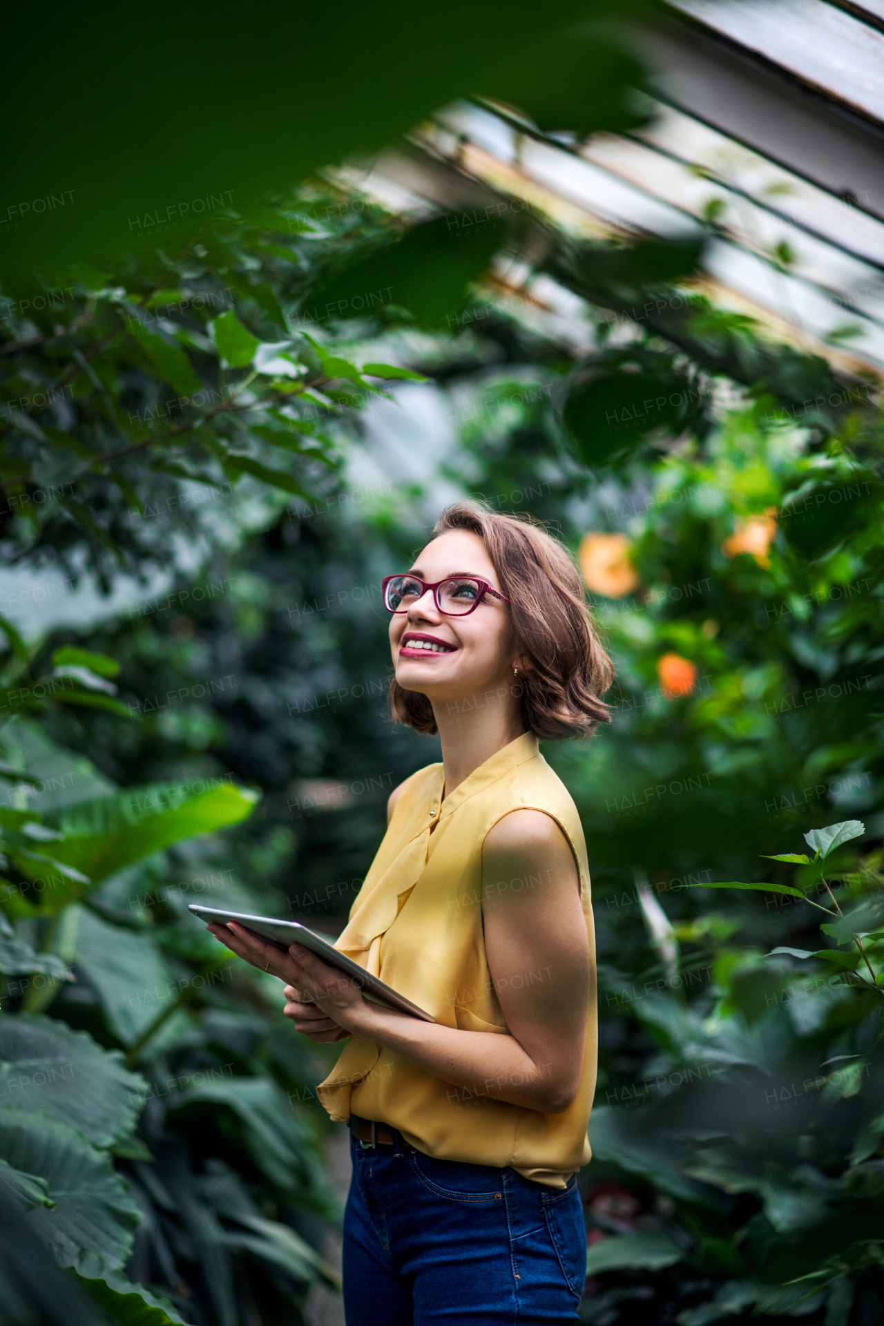 Young woman with tablet standing in greenhouse in botanical garden. Copy space.