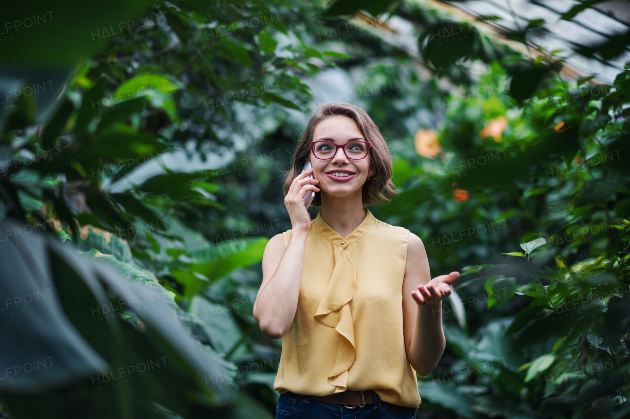 Young woman with smartpone standing in greenhouse in botanical garden. Copy space.