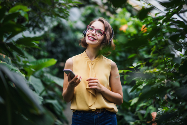 Young woman with smartpone standing in greenhouse in botanical garden. Copy space.