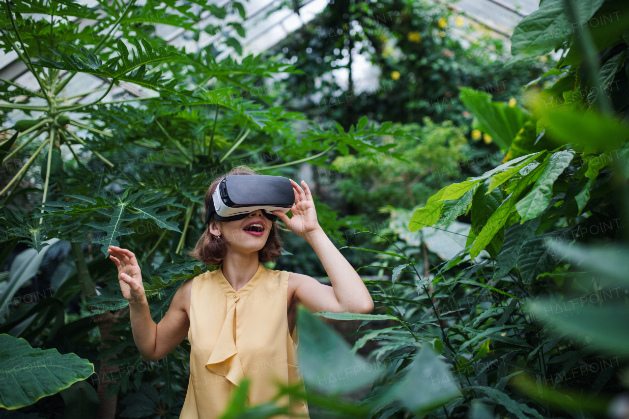 A front view of young woman standing in botanical garden, using VR glasses.