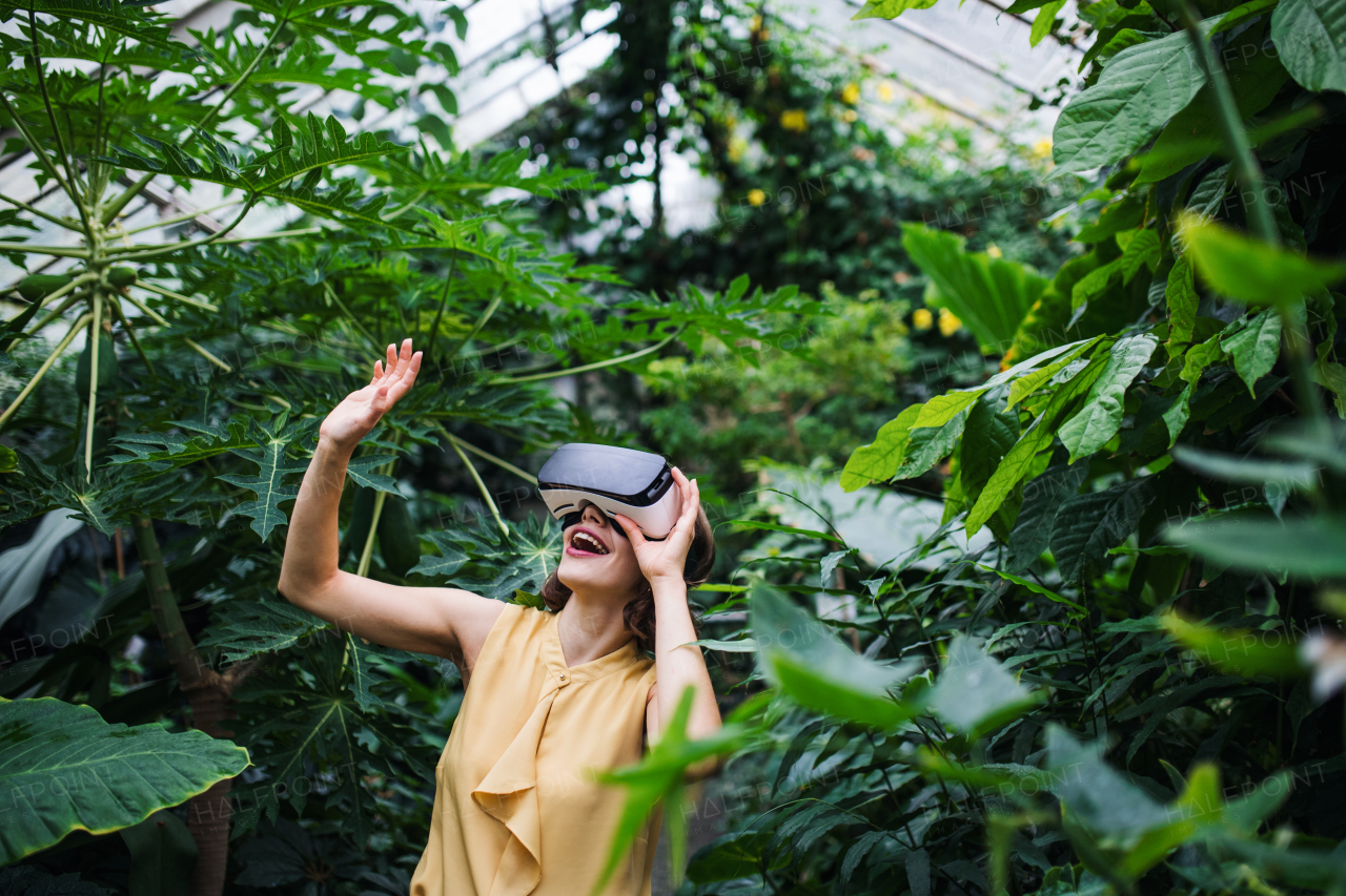 A front view of young woman standing in botanical garden, using VR glasses.