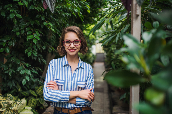 Young woman with arm crossed standing in botanical garden, looking at camera.