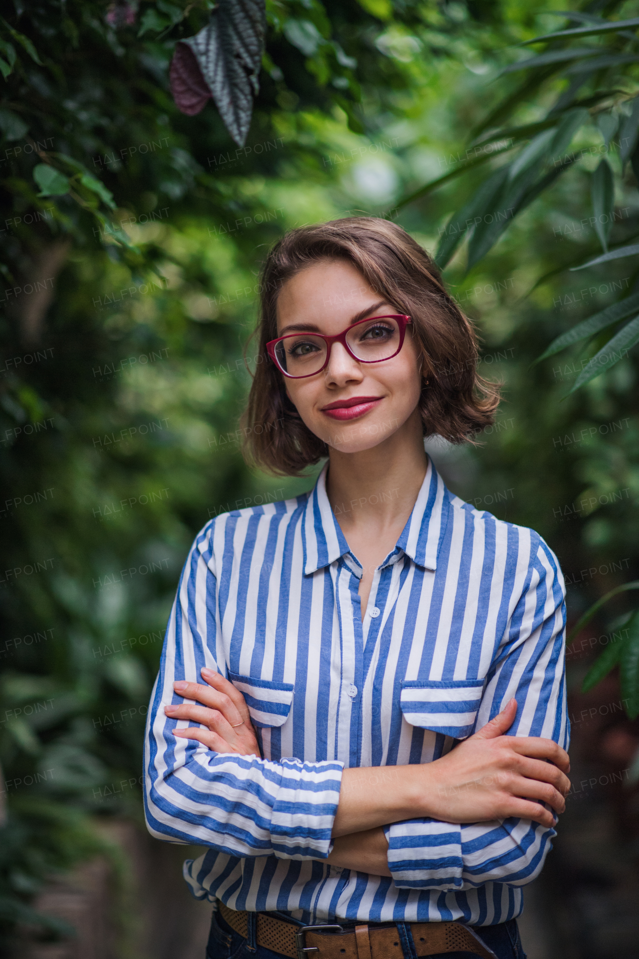 Young woman with arm crossed standing in botanical garden, looking at camera.