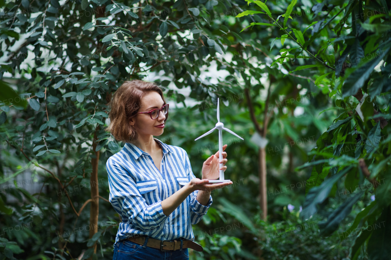 Young woman standing in botanical garden, holding windmill model. Copy space.