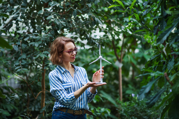 Young woman standing in botanical garden, holding windmill model. Copy space.