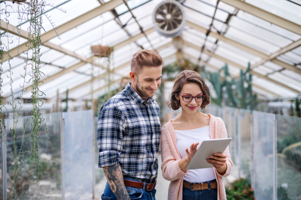 Man and woman researchers standing in greenhouse in botanical garden, using tablet.