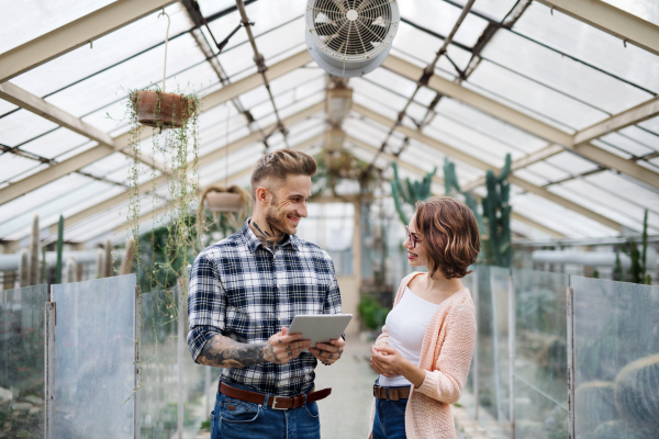 Man and woman researchers standing in greenhouse in botanical garden, using tablet.