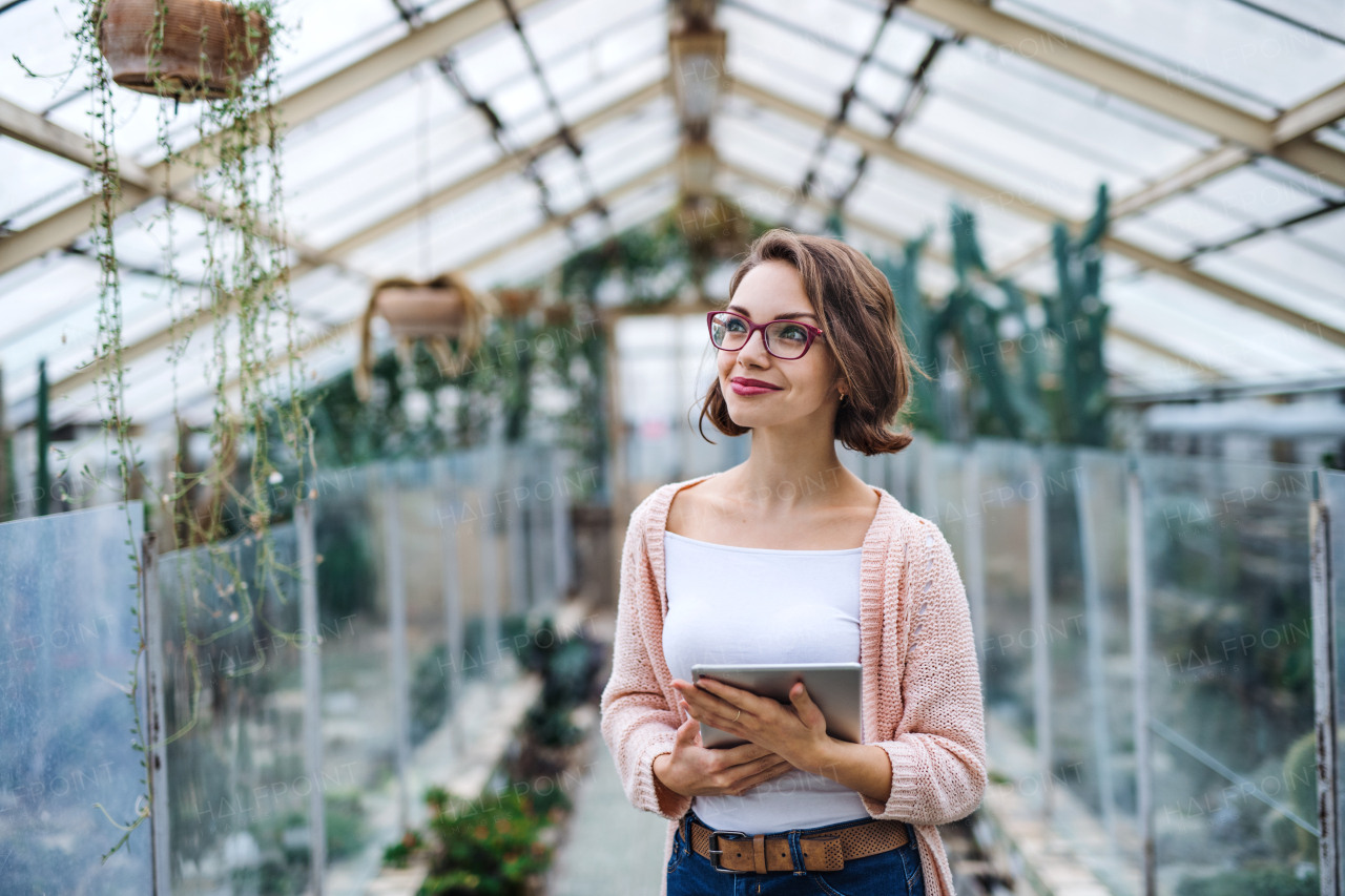 Young woman researcher standing in greenhouse in botanical garden, using tablet.