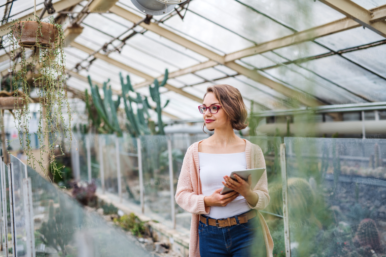 Young woman researcher standing in greenhouse in botanical garden, using tablet.