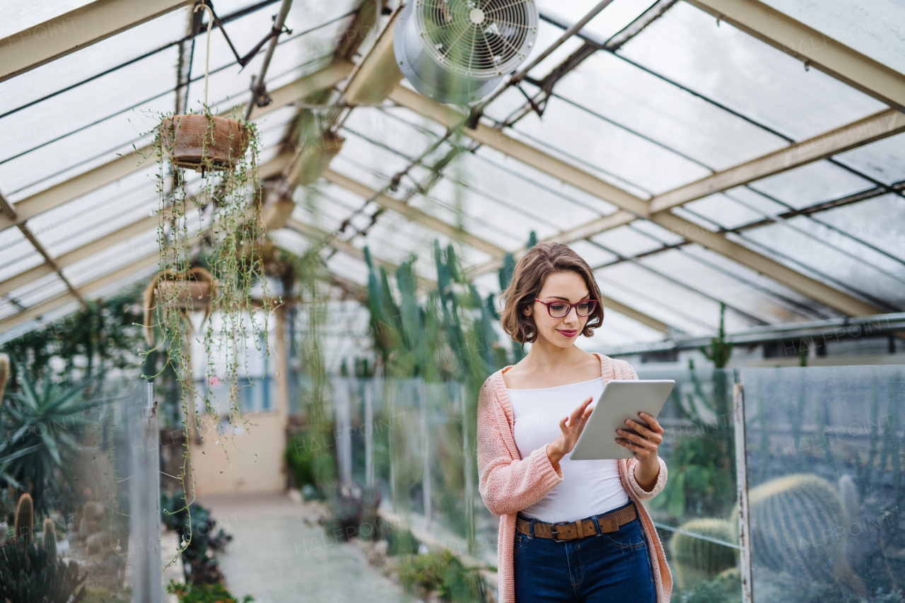 Young woman researcher standing in greenhouse in botanical garden, using tablet.