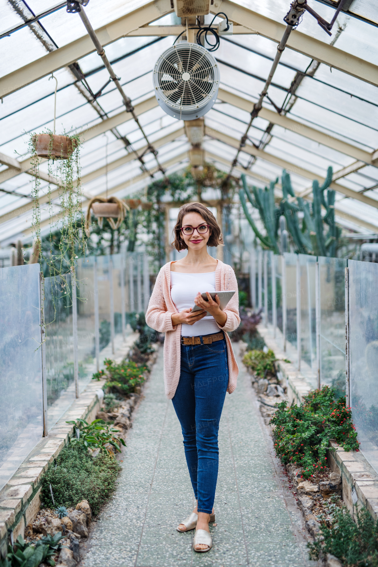 Young woman researcher standing in greenhouse in botanical garden, using tablet.