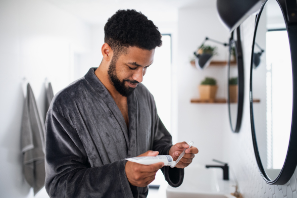 Happy young man brushing teeth indoors at home, morning or evening routine concept.