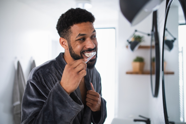 Happy young man brushing teeth indoors at home, morning or evening routine concept.