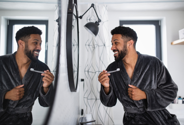 Happy young man brushing teeth indoors at home, morning or evening routine concept.