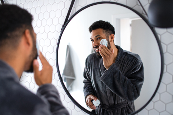 Portrait of young man using shaving gel indoors at home, morning or evening routine concept.