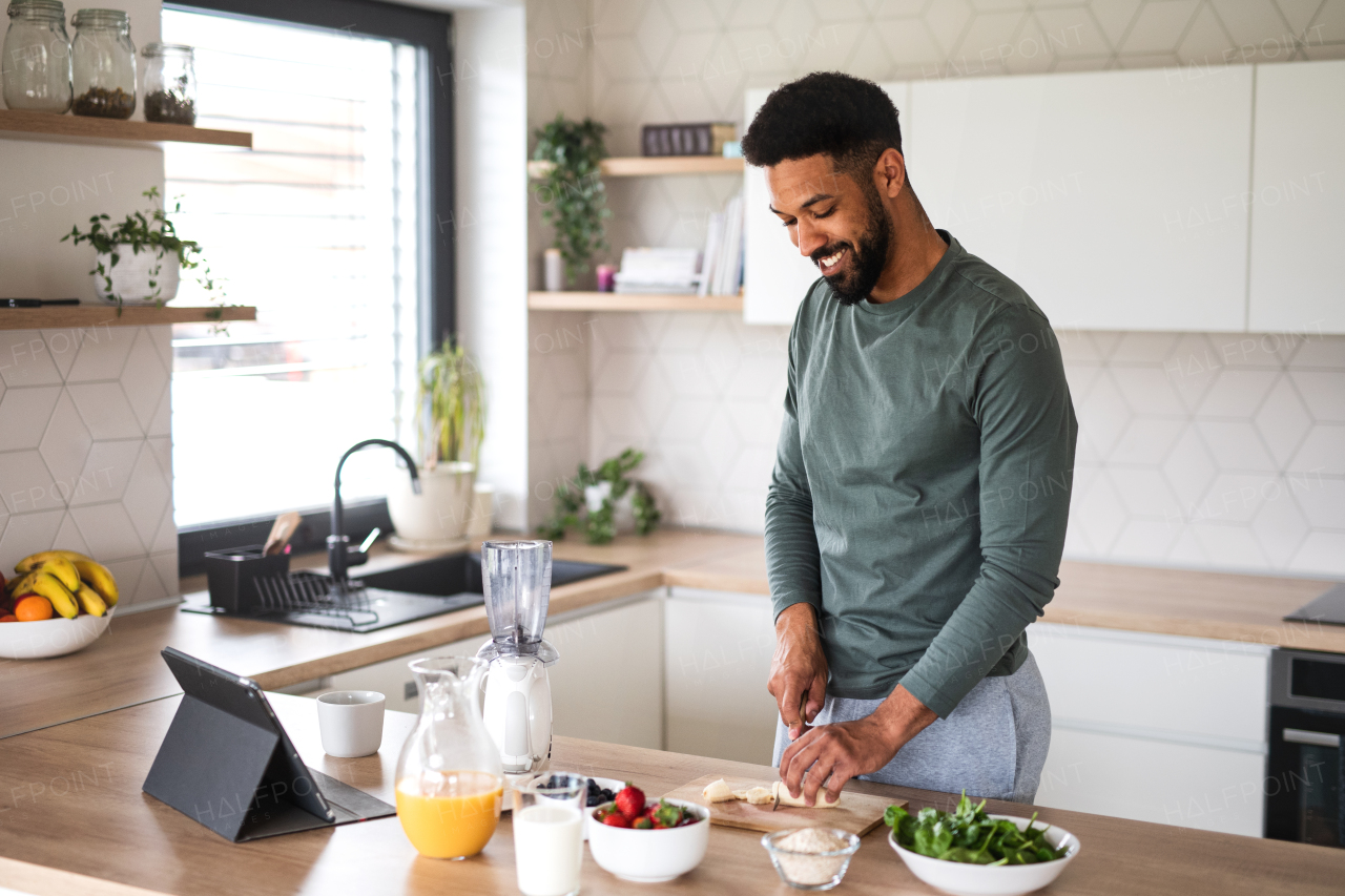 Portrait of young man with tablet preparing healthy breakfast indoors at home, home office concept.