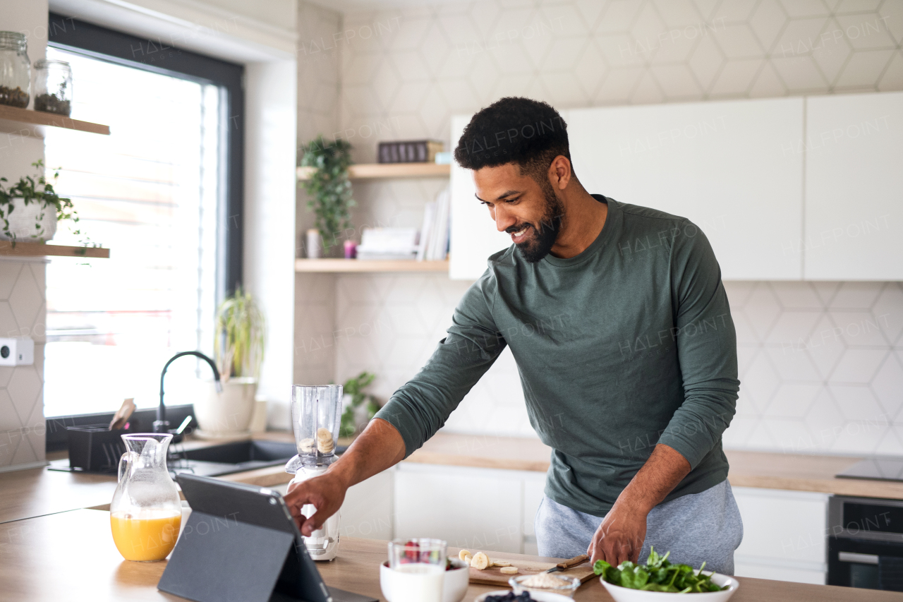 Portrait of young man with tablet preparing healthy breakfast indoors at home, home office concept.