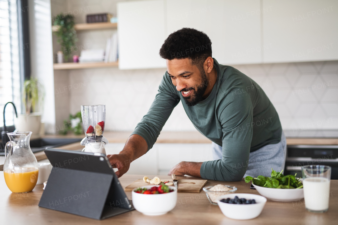 Portrait of young man with tablet preparing healthy breakfast indoors at home, home office concept.