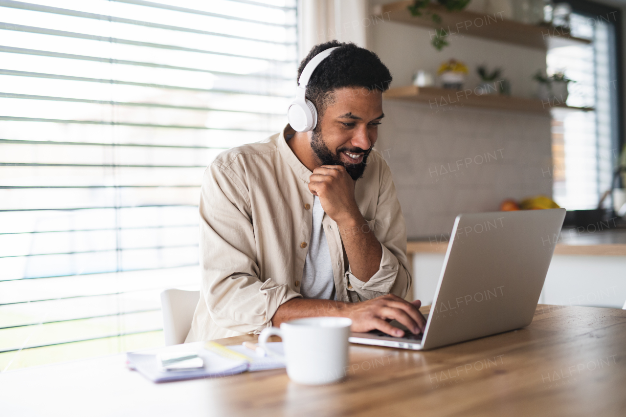 Portrait of young man student with laptop and headphones indoors at home, studying.