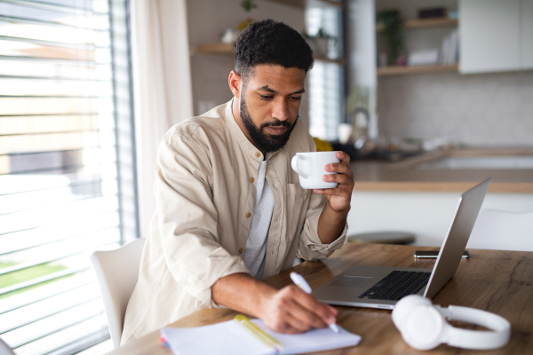 A young man student with laptop working indoors at home, home office concept.