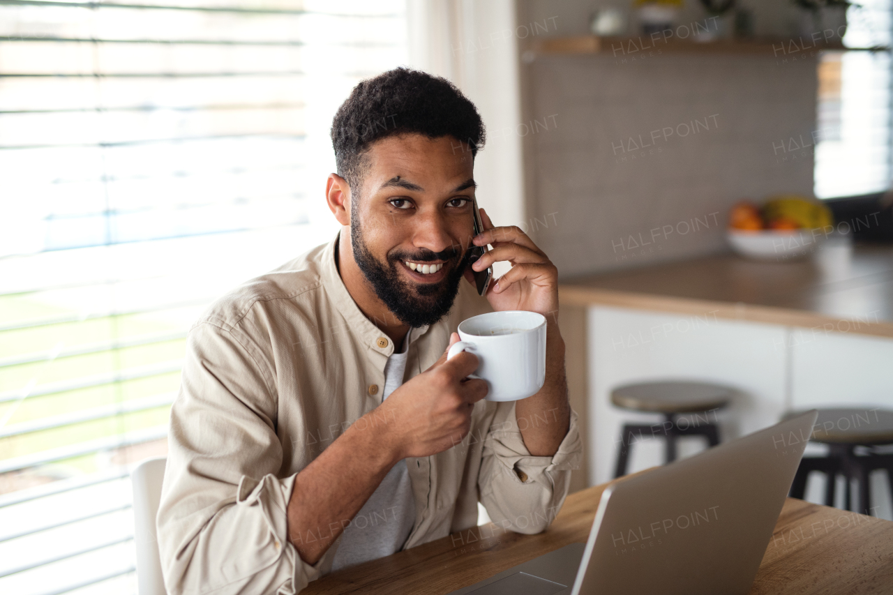 Happy young man student with laptop and smartphone working indoors at home, home office concept.