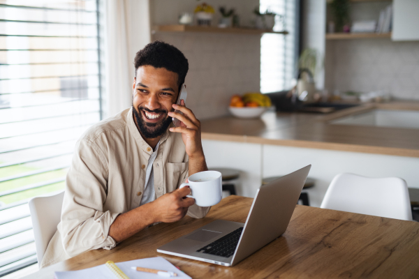 Happy young man student with laptop and smartphone working indoors at home, home office concept.