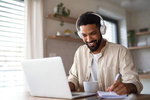 Portrait of young man student with laptop and headphones indoors at home, studying.