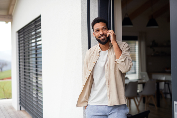 Portrait of young man student with smartphone outdoors on patio at home, making a phone call.