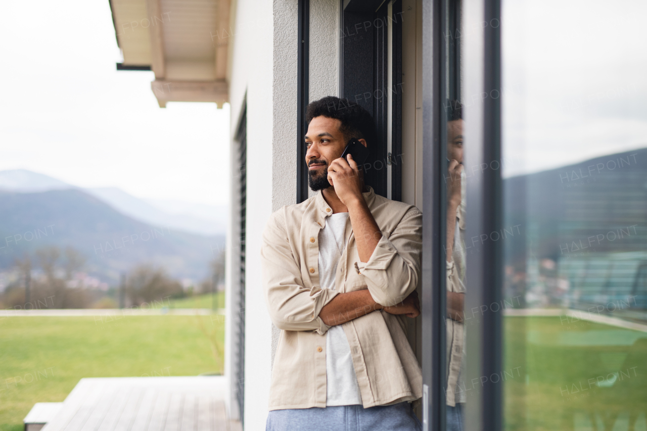 Portrait of young man student with smartphone outdoors on patio at home, making a phone call.