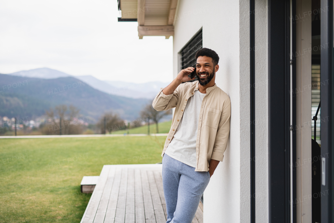 Portrait of young man student with smartphone outdoors on patio at home, making a phone call.