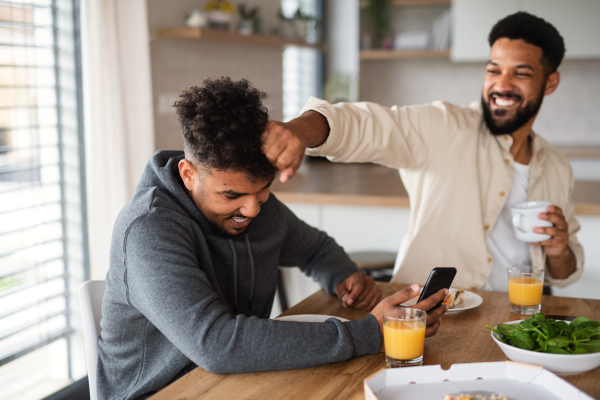 A portrait of young adult brothers in kitchen indoors at home, having fun when eating pizza.