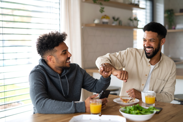 A portrait of young adult brothers in kitchen indoors at home, having fun when eating pizza.