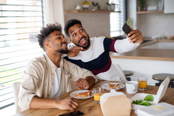 A portrait of young adult brothers in kitchen indoors at home, taking selfie.