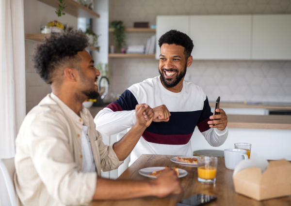 A portrait of young adult brothers in kitchen indoors at home, having fun when eating pizza.