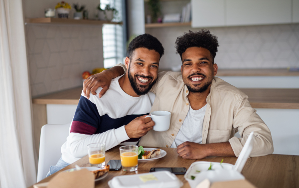 A portrait of young adult brothers with pizza in kitchen indoors at home, looking at camera.