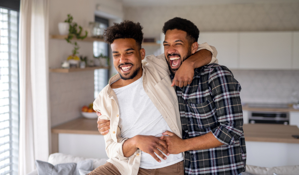 Young laughing adult brothers in kitchen indoors at home, having fun.