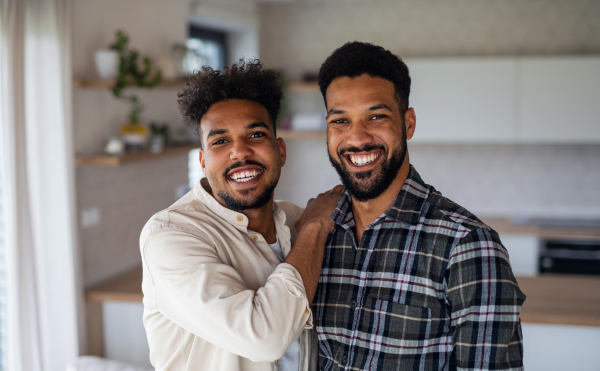 Portrait of young adult brothers in kitchen indoors at home, looking at camera.