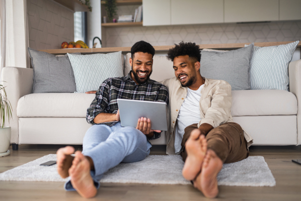 Portrait of young student brothers in kitchen indoors at home, using tablet and laughing.