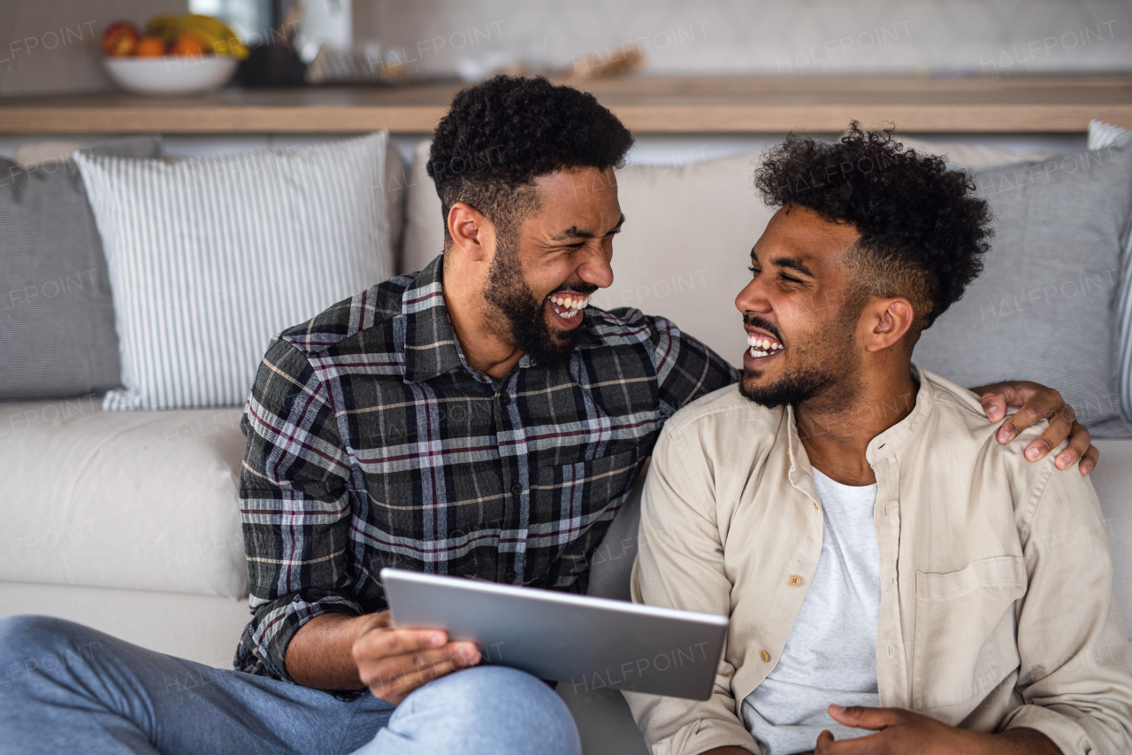 Portrait of young student brothers in kitchen indoors at home, using tablet and laughing.