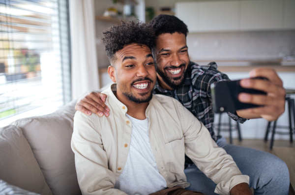 A portrait of young adult brothers on sofa indoors at home, taking selfie.