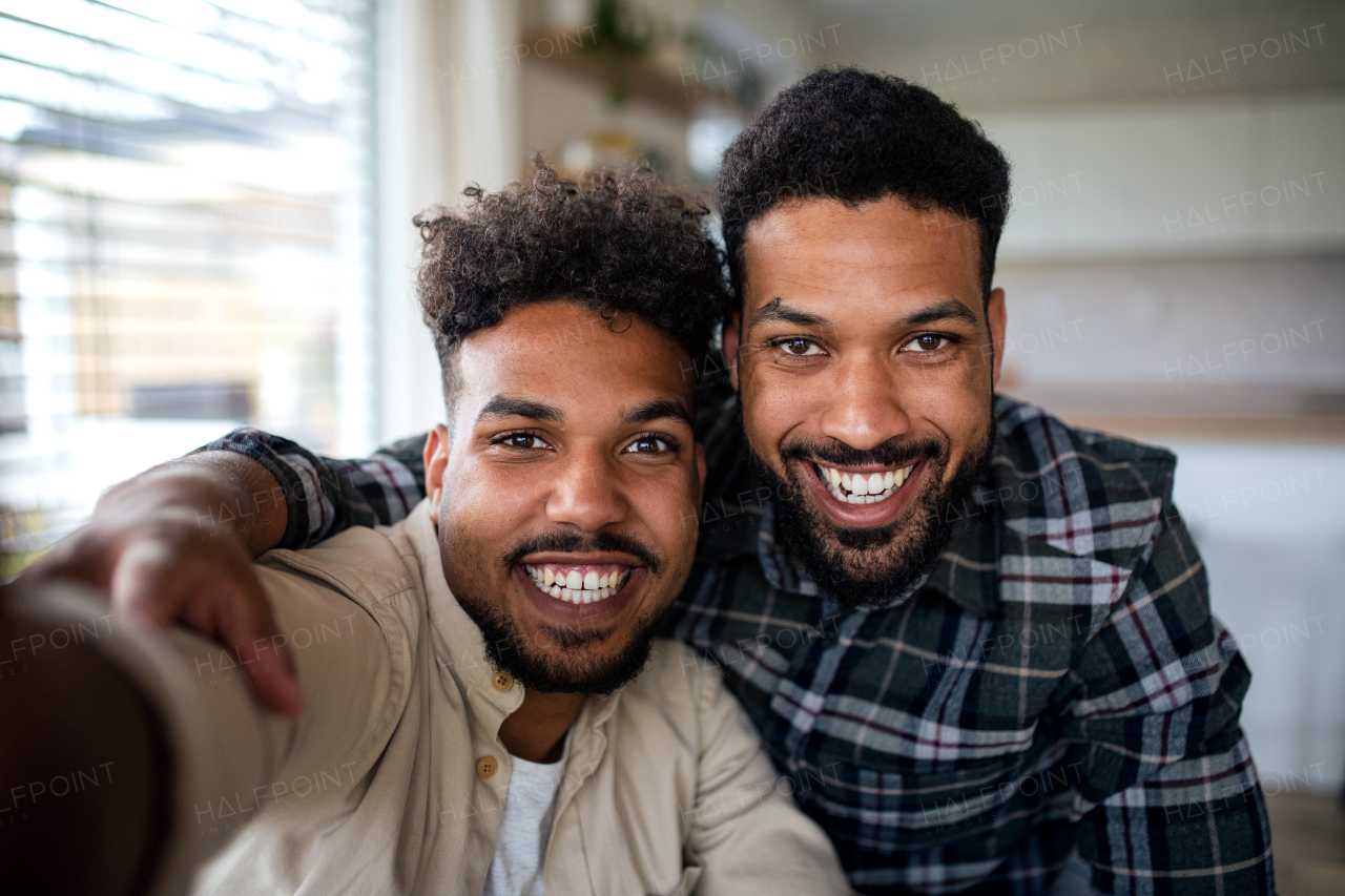 A portrait of young adult brothers in kitchen indoors at home, taking selfie.