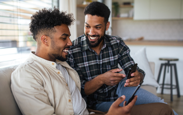 Portrait of young student brothers in kitchen indoors at home, using smartphone.