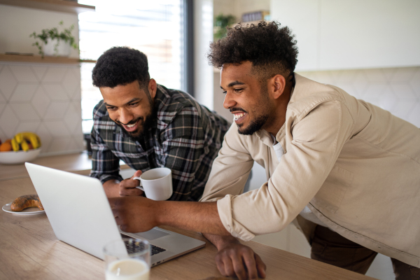 Portrait of young student brothers in kitchen indoors at home, using laptop.