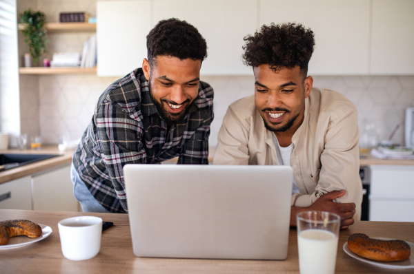 Portrait of young student brothers in kitchen indoors at home, using laptop.